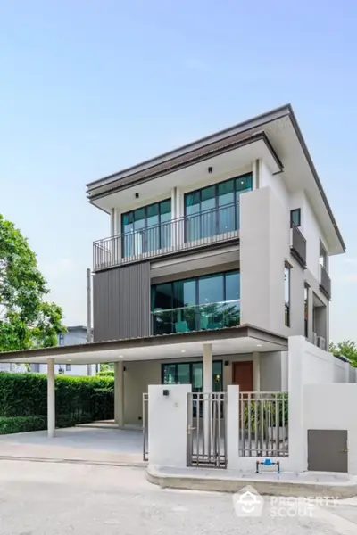 Modern three-story house with large windows and balcony in a serene neighborhood.