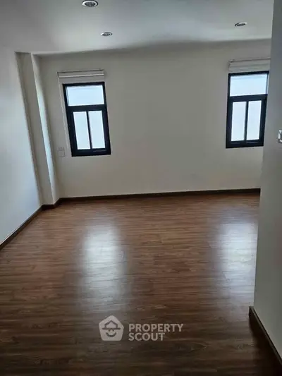 Spacious empty room with wooden flooring and large windows, perfect for customization.