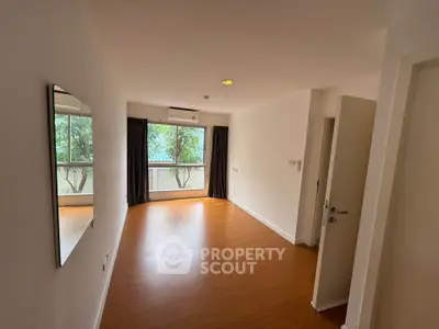 Spacious empty room with large window and wooden flooring, ideal for customization.