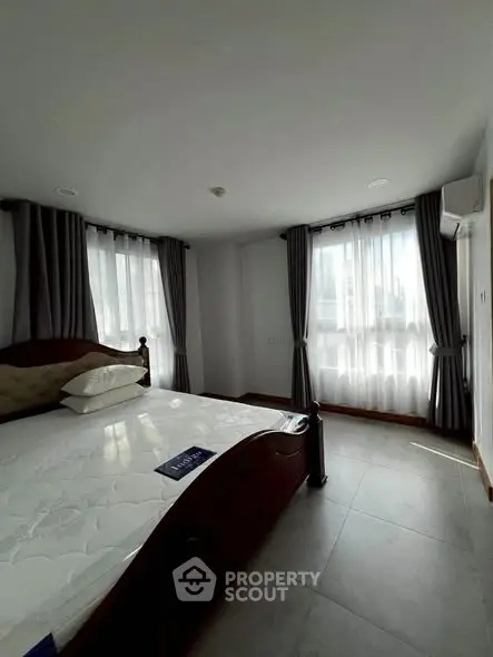 Spacious bedroom with large windows and elegant curtains in a modern apartment.
