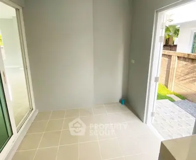 Bright empty room with tiled floor and sliding glass door leading to a small garden area.