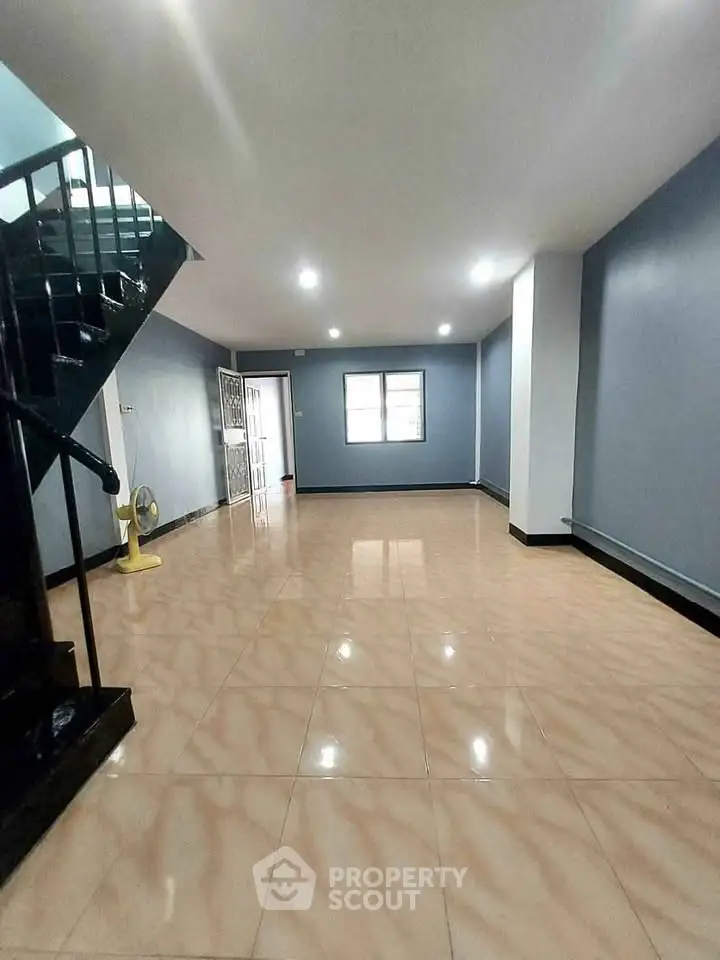 Spacious empty living room with tiled flooring and staircase, ideal for customization.