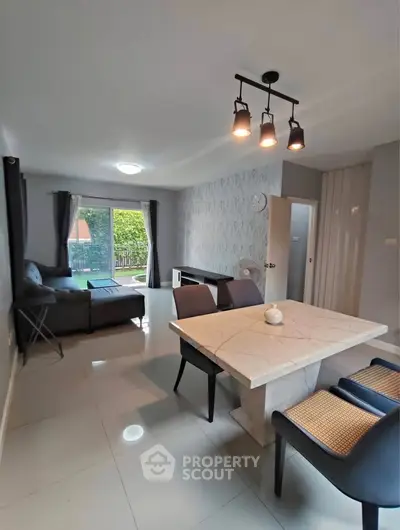 Modern living room with stylish dining area and cozy seating, featuring elegant lighting and large windows.