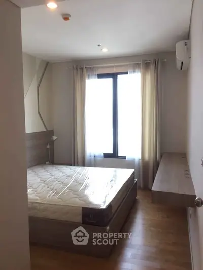Cozy bedroom with natural light, wooden flooring, and modern furnishings in a stylish apartment.
