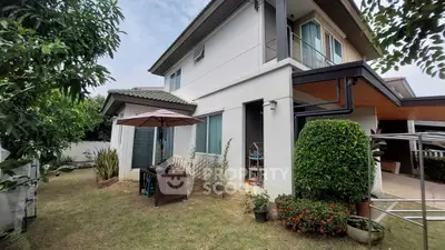 Charming two-story home with lush garden and cozy outdoor seating area, perfect for family gatherings.