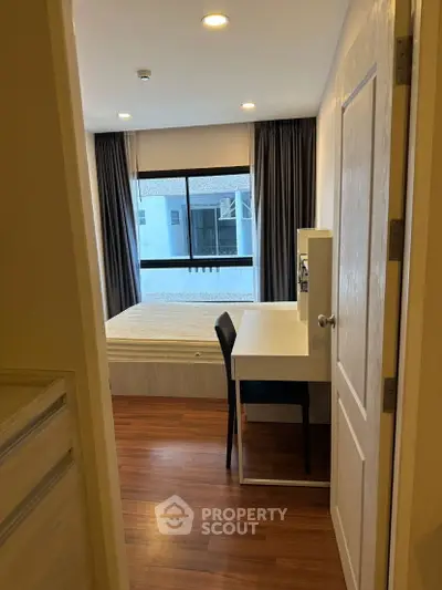 Cozy bedroom with wooden flooring and study desk, featuring large window for natural light.