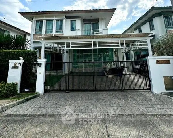 Modern two-story house with gated driveway and lush greenery.