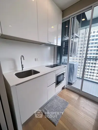 Modern compact kitchen with sleek white cabinets and balcony view in urban apartment