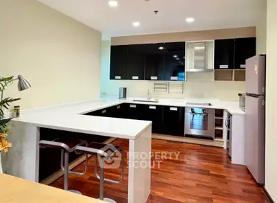 Modern kitchen with sleek black cabinets and hardwood floors, featuring a breakfast bar and stainless steel appliances.