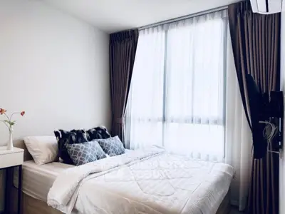 Cozy bedroom with large window and elegant curtains, featuring a comfortable bed and stylish decor.