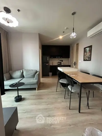 Modern open-layout living room with dining area and kitchen, featuring sleek furniture and neutral tones.
