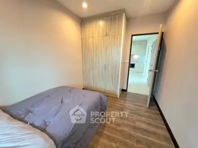 Cozy bedroom with wooden flooring and built-in wardrobe, leading to a modern kitchen.