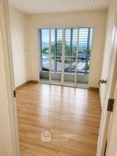 Bright empty room with wooden flooring and large windows offering scenic views.