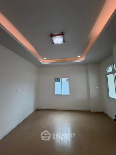 Spacious empty room with modern ceiling lights and natural light from windows.
