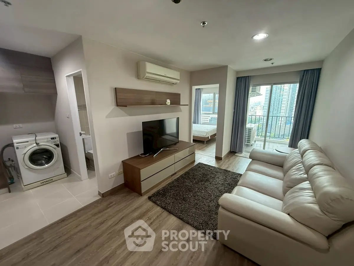 Modern living room with open layout, featuring a cozy sofa, TV, and a glimpse of the bedroom and balcony view.