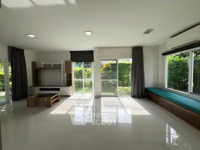 Spacious living room with large windows and garden view, featuring modern furniture and ample natural light.