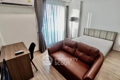 Modern studio apartment with cozy sofa, bed, and work desk near large window.