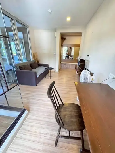 Modern living room with wooden flooring and glass partition, featuring a cozy sofa and study desk.