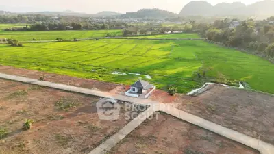 Scenic aerial view of a small house surrounded by lush green fields and mountains, perfect for tranquil living.