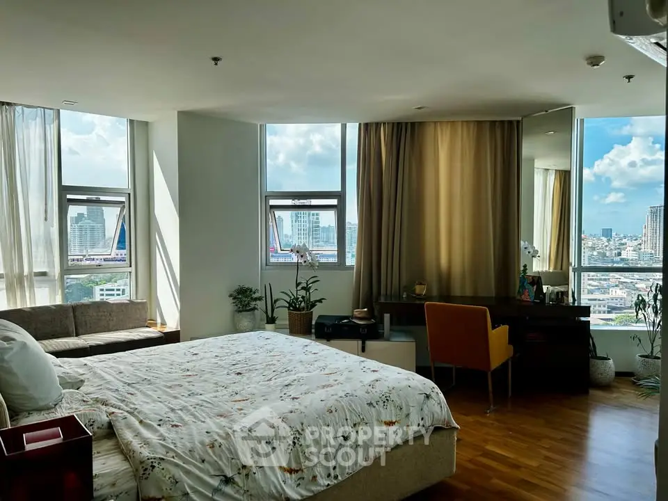 Spacious bedroom with city view, featuring cozy seating area and elegant decor.