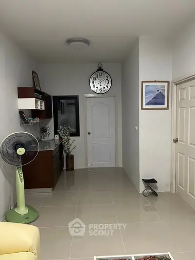 Modern living room with sleek design, featuring a wall clock, fan, and decorative shelves.