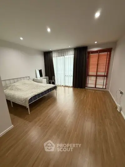 Spacious bedroom with wooden flooring and large window, perfect for natural light.