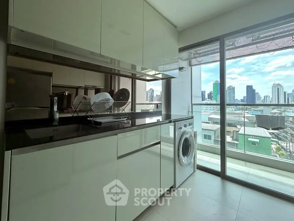 Modern kitchen with sleek cabinets and city view from large window, featuring a washing machine.