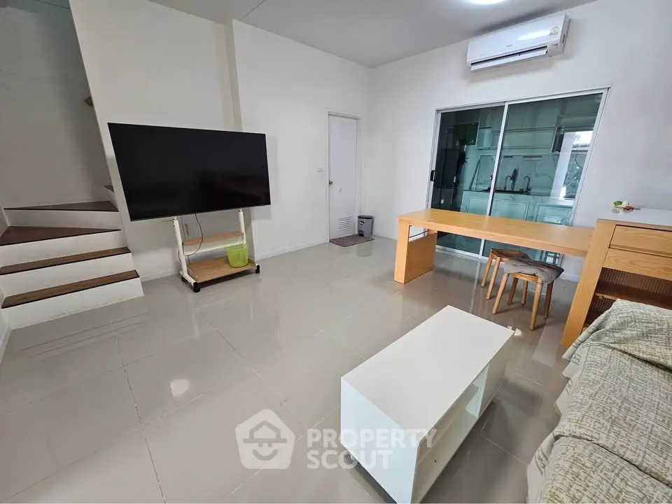 Modern living room with sleek design, featuring a large TV, stylish furniture, and air conditioning.