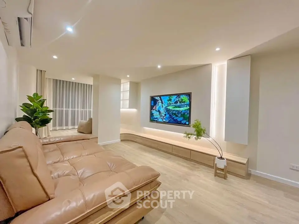 Modern living room with sleek design and large TV, featuring cozy leather seating and stylish decor.