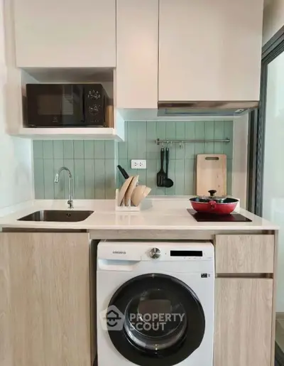 Modern compact kitchen with washing machine and microwave, featuring sleek cabinetry and stylish backsplash.