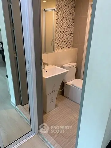 Modern compact bathroom with stylish sink and mosaic tile accent wall.