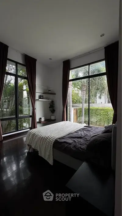 Luxurious bedroom with large windows and garden view, featuring elegant dark curtains and cozy bedding.