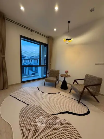 Modern living room with stylish chairs and large window offering a view of neighboring houses.