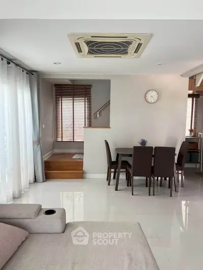Modern living room with dining area, featuring sleek furniture and large windows for natural light.