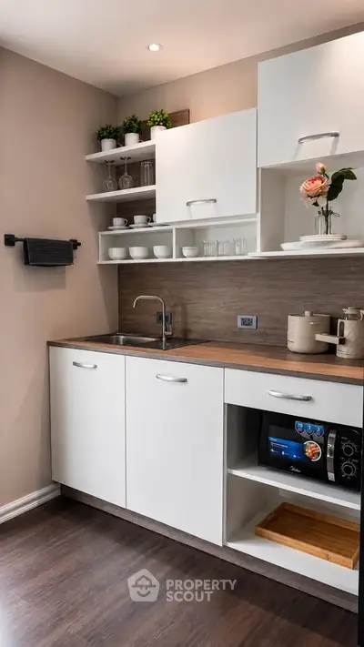 Modern kitchen with sleek white cabinets and wooden countertop, featuring a microwave and stylish open shelving.