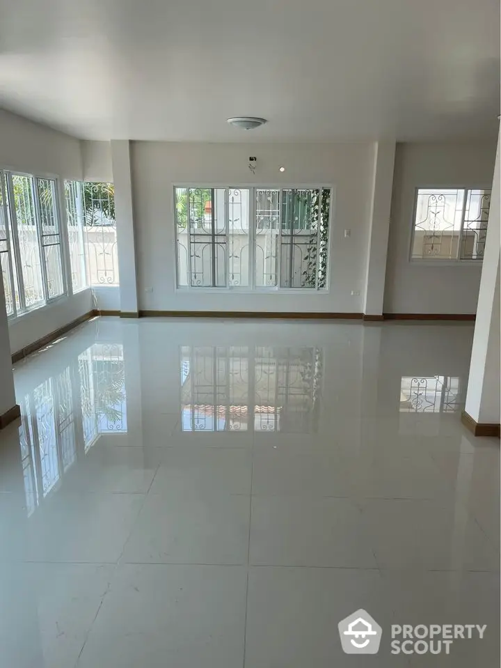 Spacious and sunlit living room with gleaming tiled floors, large windows with protective grills, and ample natural light, perfect for family gatherings and entertaining guests.