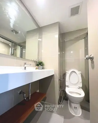 Modern bathroom with sleek fixtures and neutral tiles, featuring a spacious mirror and elegant design.