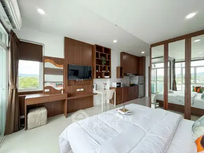 Modern studio apartment with open layout, featuring a cozy bed, sleek kitchen, and scenic balcony view.