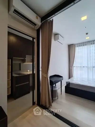 Modern studio apartment with sleek kitchen and cozy bedroom, featuring large windows and elegant curtains.