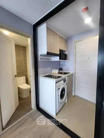 Compact modern kitchen with washing machine and adjacent bathroom in stylish apartment.
