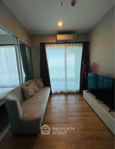 Cozy living room with modern sofa and large TV, featuring natural light from balcony.