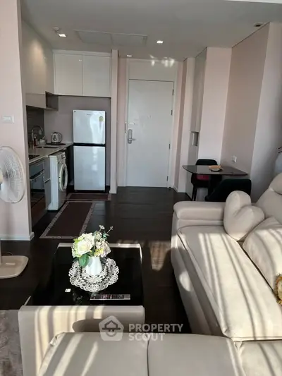 Modern living room with open kitchen, featuring sleek furniture and natural light.