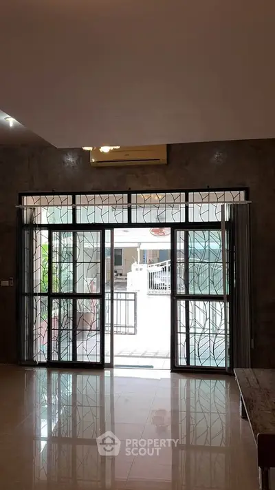 Spacious living room with large glass doors opening to a bright outdoor area, featuring elegant metalwork design.