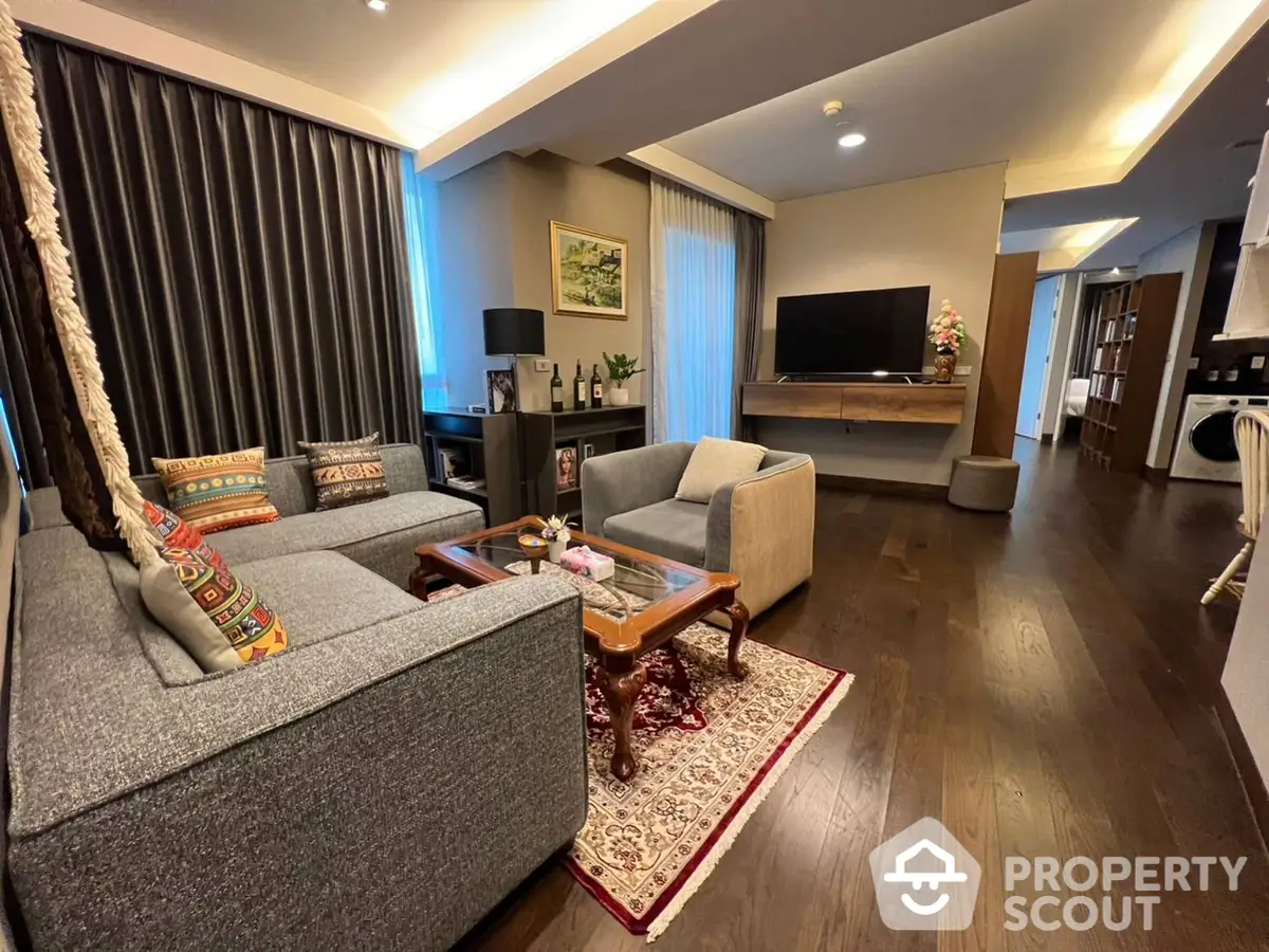 Spacious living room with elegant hardwood flooring, plush sofas, and modern entertainment unit, seamlessly connecting to an open-plan kitchen area.