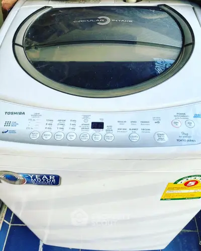 Modern washing machine with circular intake and digital controls in a tiled laundry area.