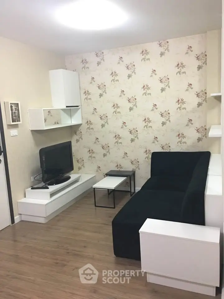 Cozy living room with modern black sofa and floral wallpaper, perfect for relaxation.