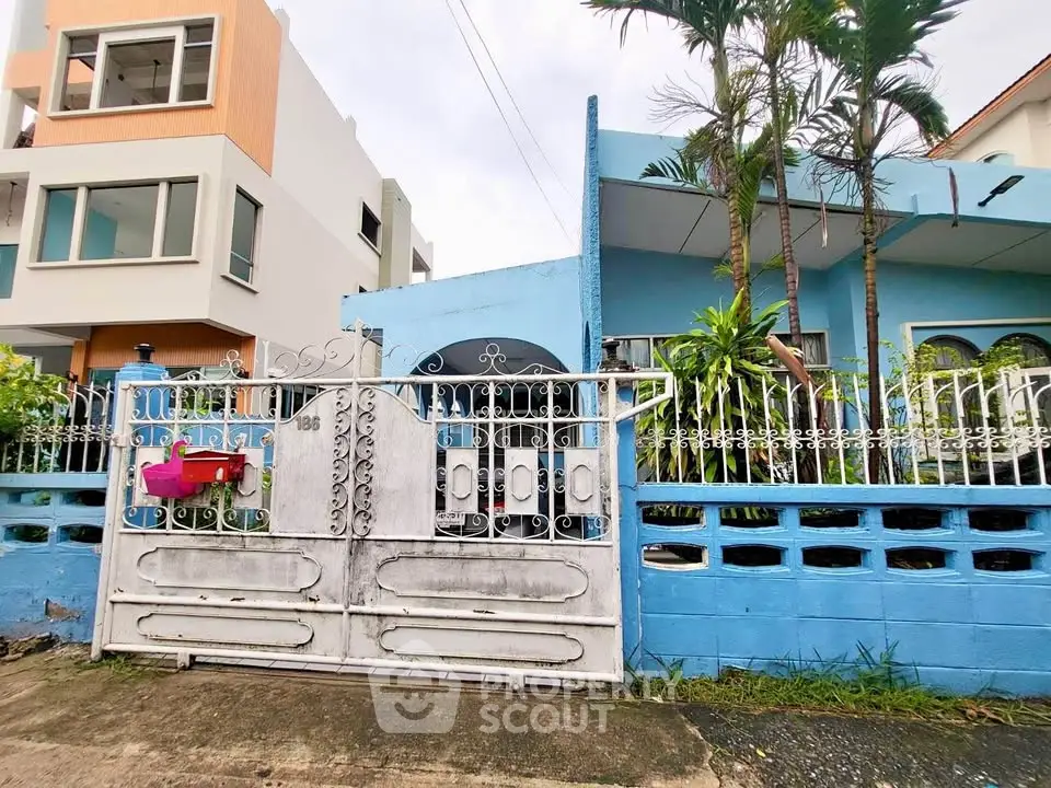 Charming blue house with lush garden and secure gated entrance in a serene neighborhood.