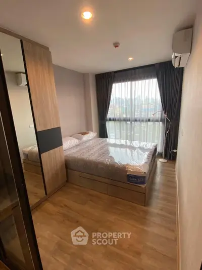 Modern bedroom with large window and wooden flooring in a stylish apartment.