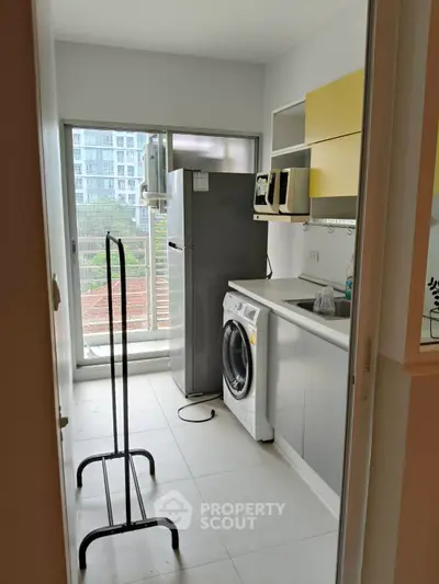 Modern kitchen with washing machine and fridge, bright natural light from balcony view.
