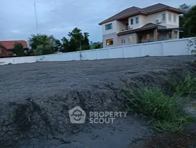 Spacious plot of land with a modern house in the background, ideal for development.